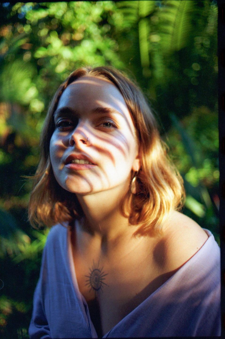 A woman with a nose ring and a chest tattoo is looking up at the camera with shadows across her face.
