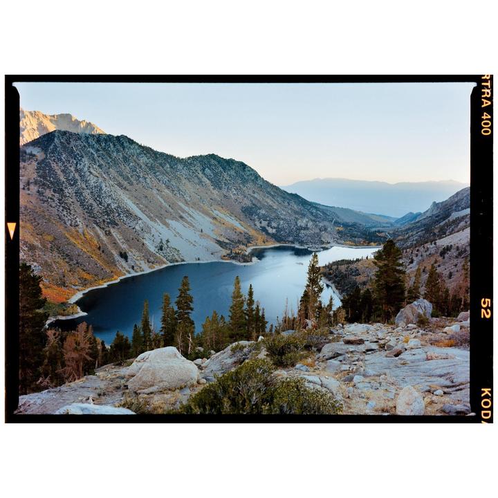 A large lake is nestled between mountains with some autumn foliage and evergreen trees.