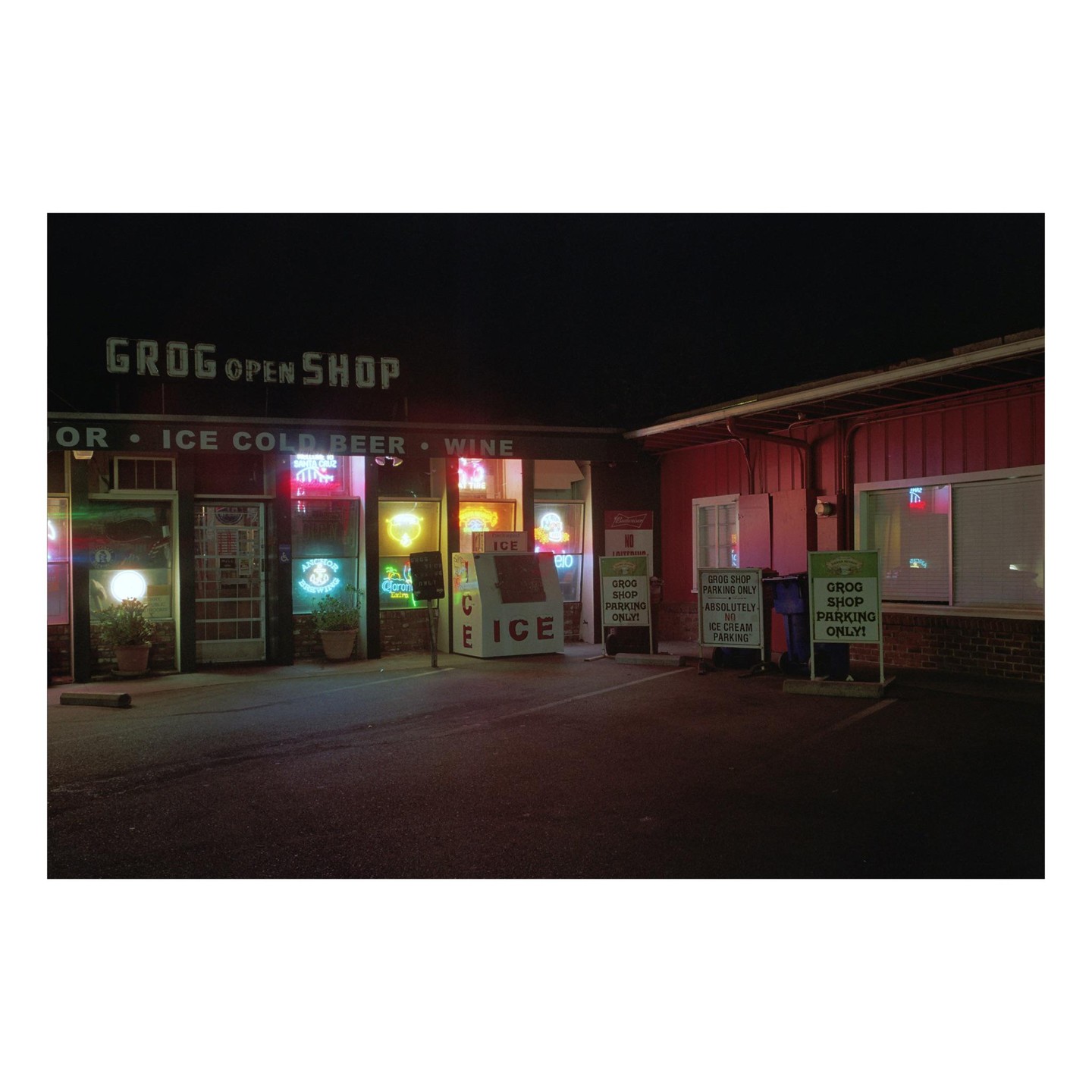 A liquor store with neon signs in the windows is illuminated at night.