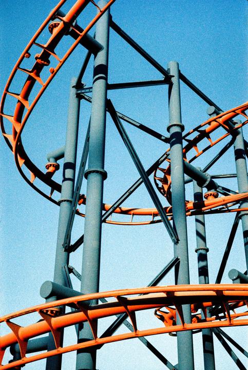 A roller coaster with orange tracks and grey supports stands against a clear blue sky.