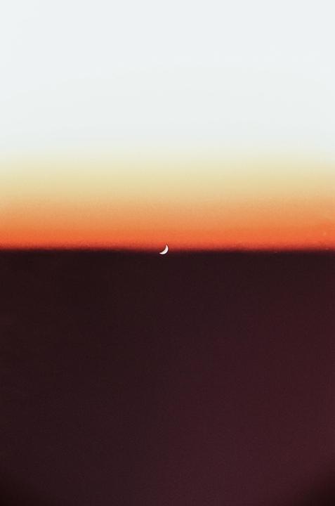 A crescent moon is visible in a gradient sky of white, orange, and dark red.