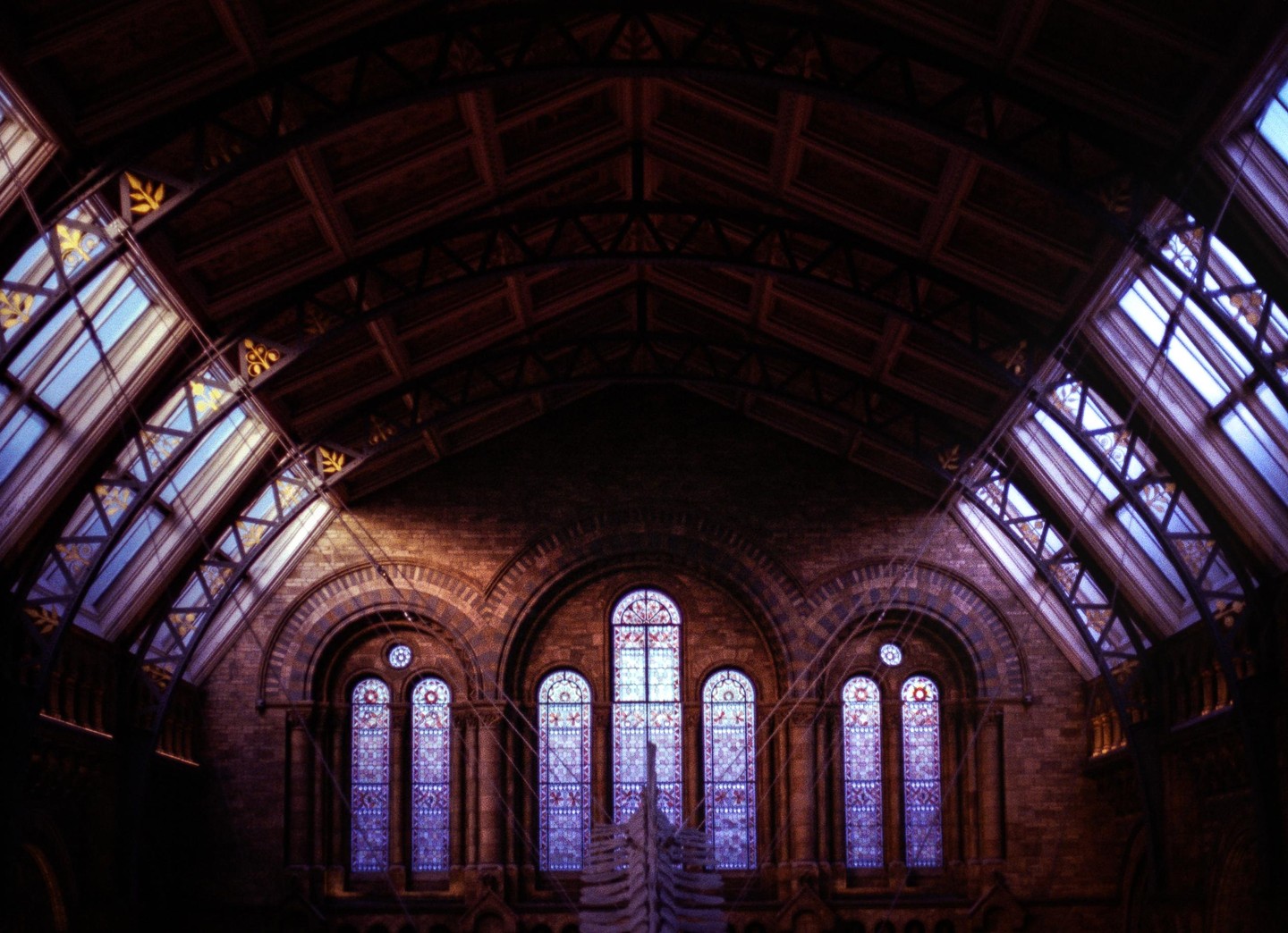 A large hall with a vaulted wooden ceiling and stained glass windows is illuminated by natural light.