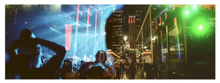 A double exposure shows a crowd at a concert with bright stage lights and a city street at night with tall buildings.
