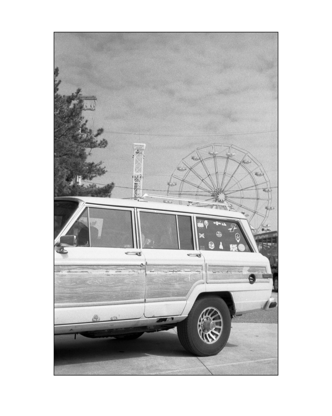 A white station wagon with wood paneling is parked in front of a ferris wheel.