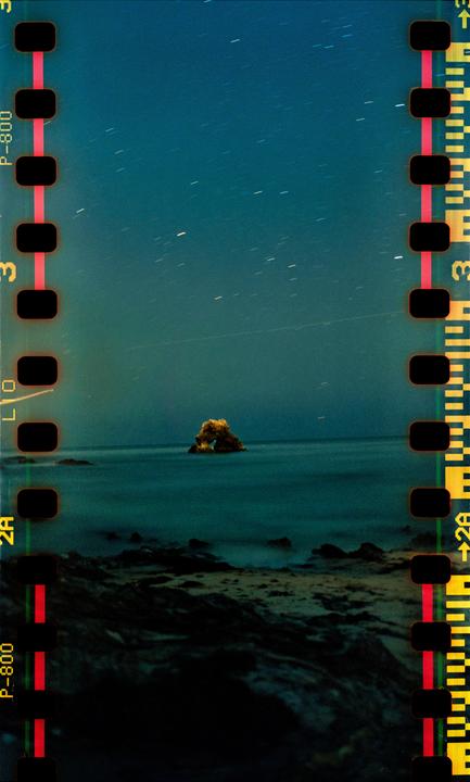 A rocky arch formation is visible in the ocean under a starry night sky.
