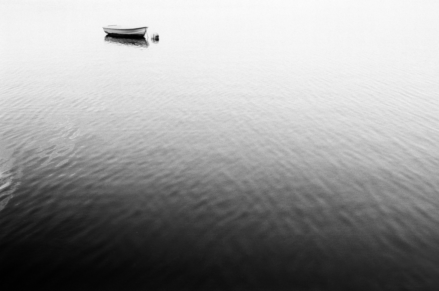 A small boat floats on calm water under a bright sky.