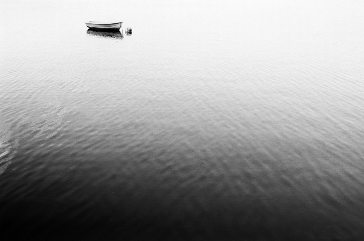 A small boat floats on calm water under a bright sky.