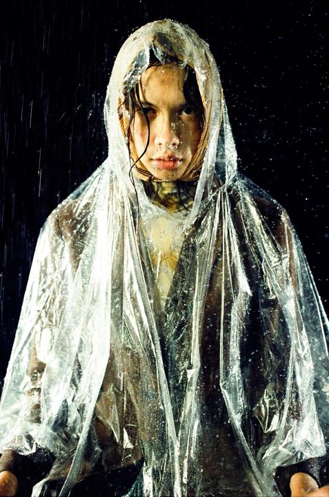 A woman wearing a clear plastic poncho stands in the rain at night.