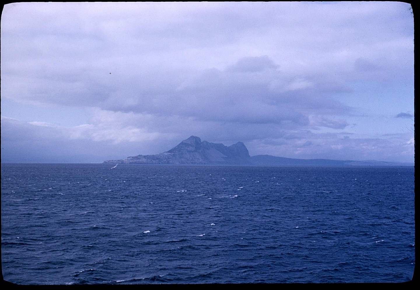 A large body of water with a mountain range in the distance under a cloudy sky.