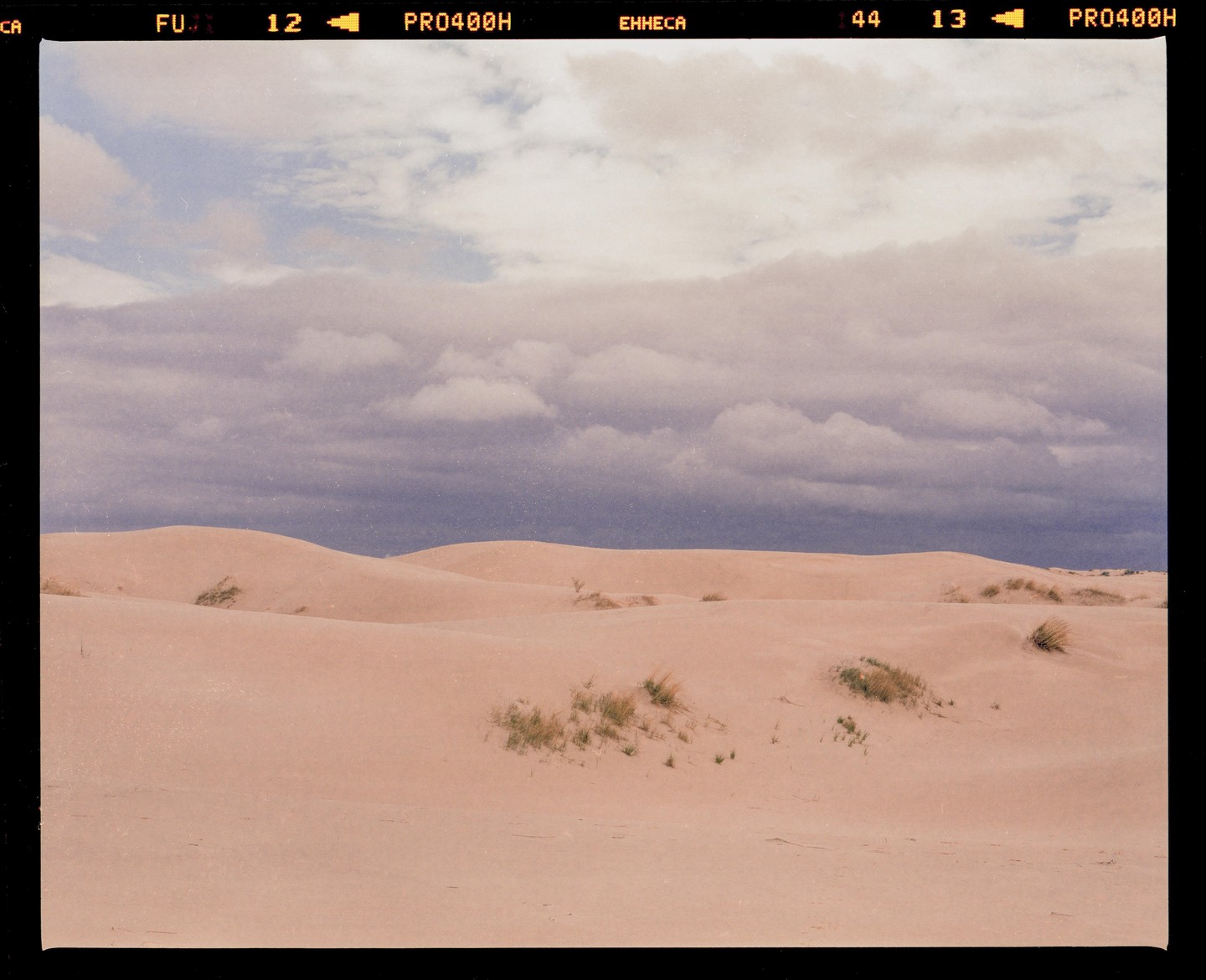 A desert landscape shows sand dunes under a cloudy sky.