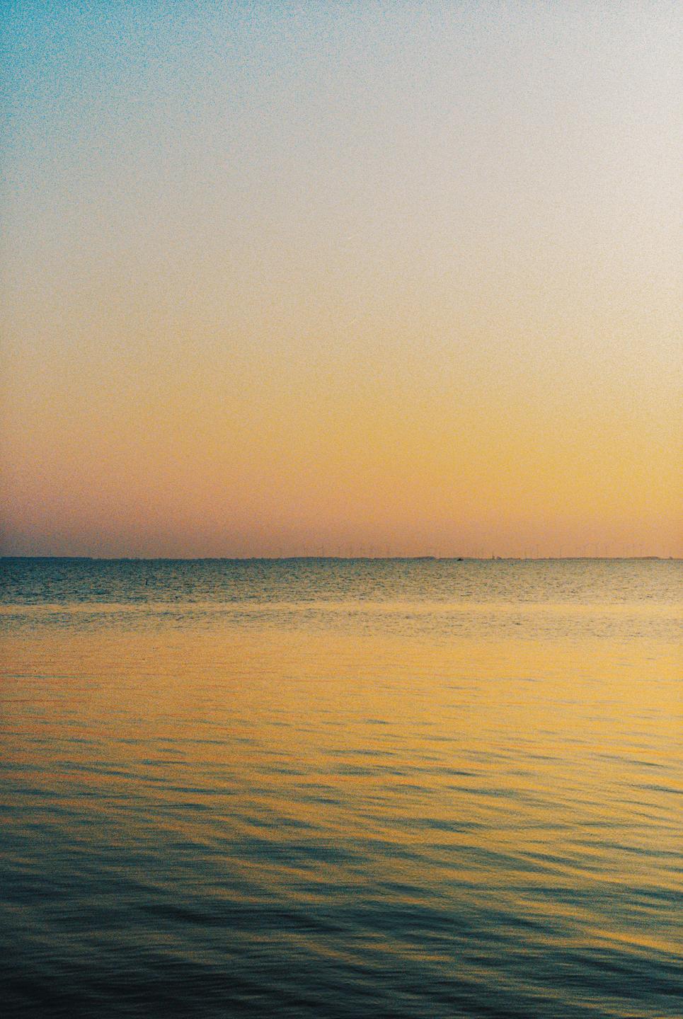 The sun sets over a calm body of water with a distant horizon.
