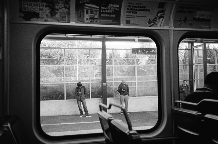 Three men stand on a light rail platform, viewed from inside a train.