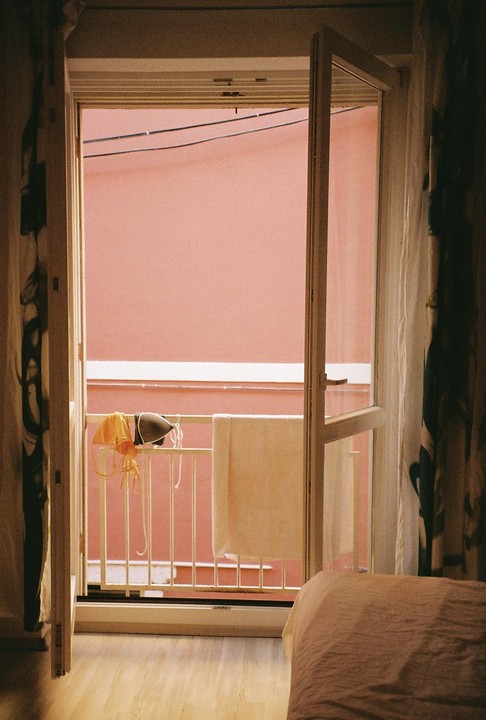 A balcony with a towel and two bikini tops hanging on the railing is visible through an open door.