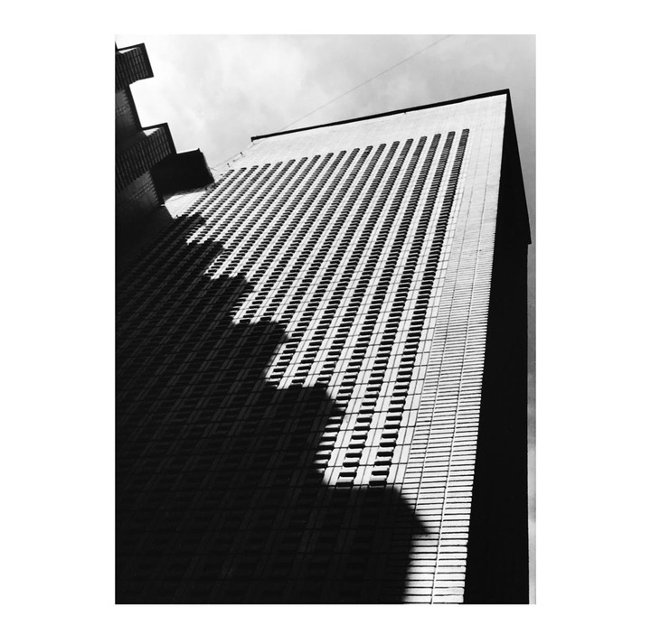 A tall building with many windows is partially covered in shadow, creating a diagonal pattern.
