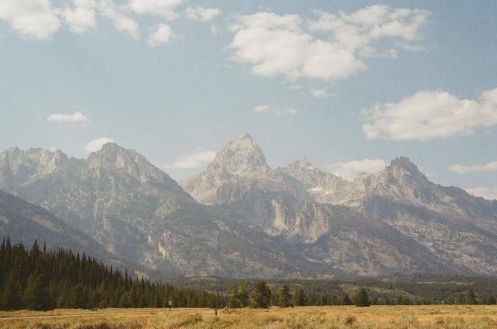 A mountain range with a forest in the foreground is visible under a hazy sky with scattered clouds.