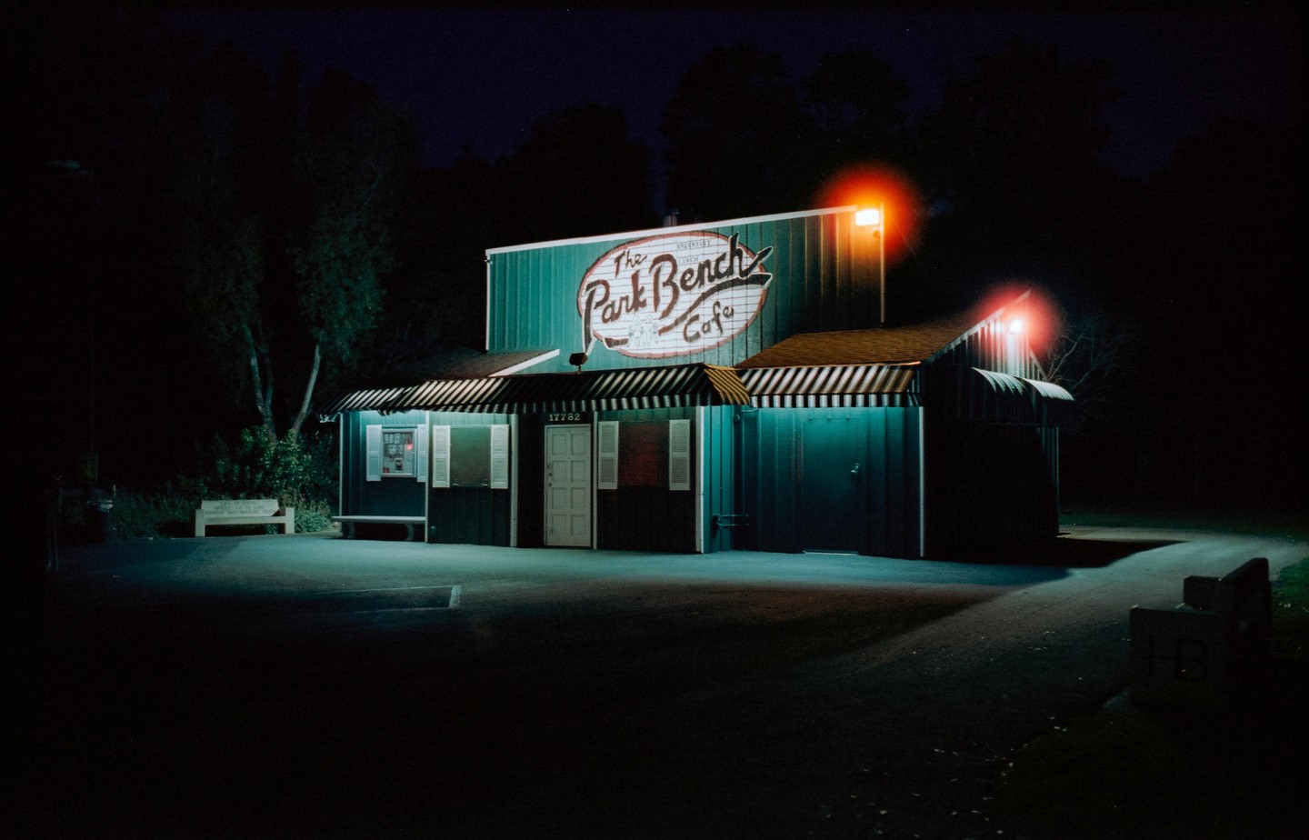 The Park Bench Cafe is illuminated at night with red lights and a striped awning.
