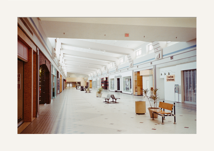 An empty shopping mall corridor stretches into the distance, lined with closed storefronts and a few benches.