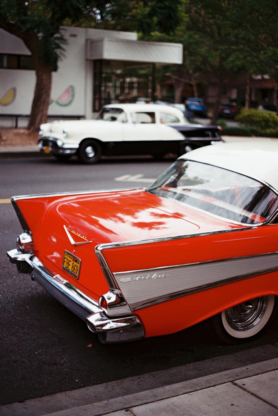 The rear of a red and white vintage car is parked on a street with another vintage car in the background.