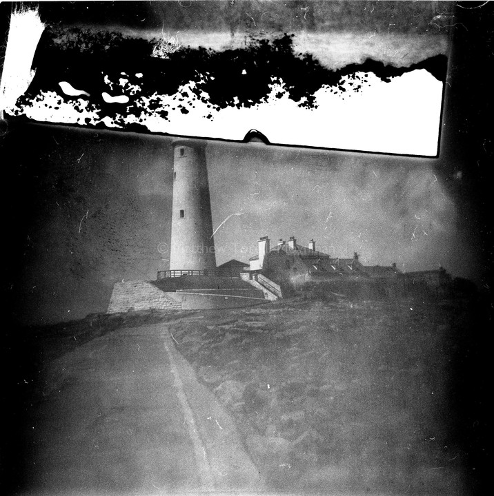A lighthouse stands on a hill next to a building, with a path leading up to it.