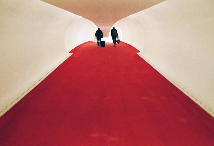 Two people walk away down a long, curving, red-carpeted hallway.