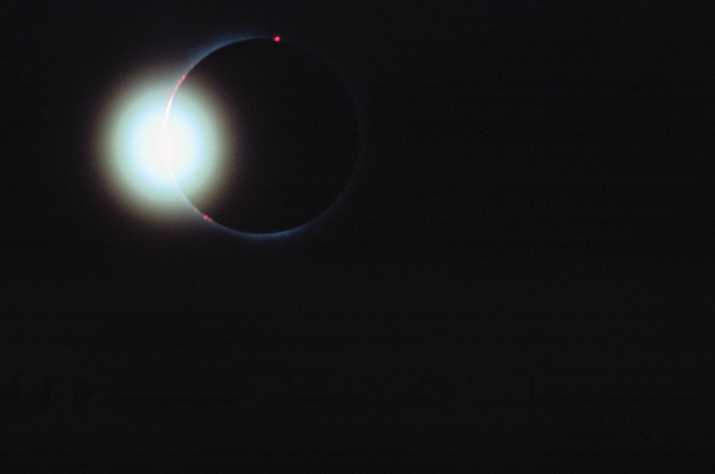 A solar eclipse is visible against a dark sky with bright light emanating from behind the moon.