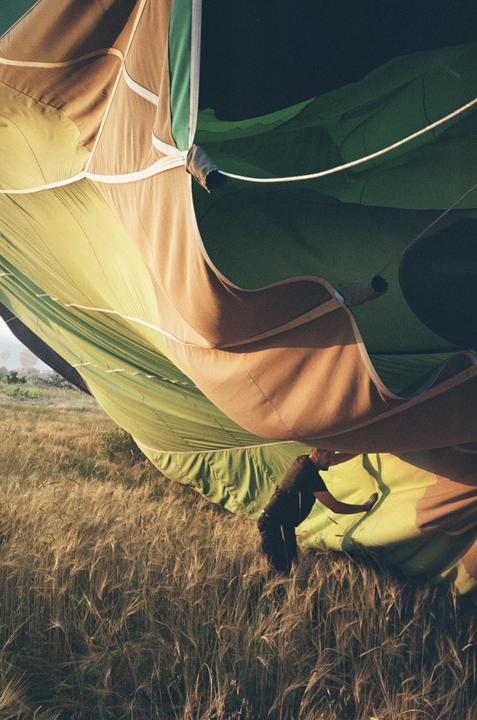 A man is working on a hot air balloon in a field of tall grass.