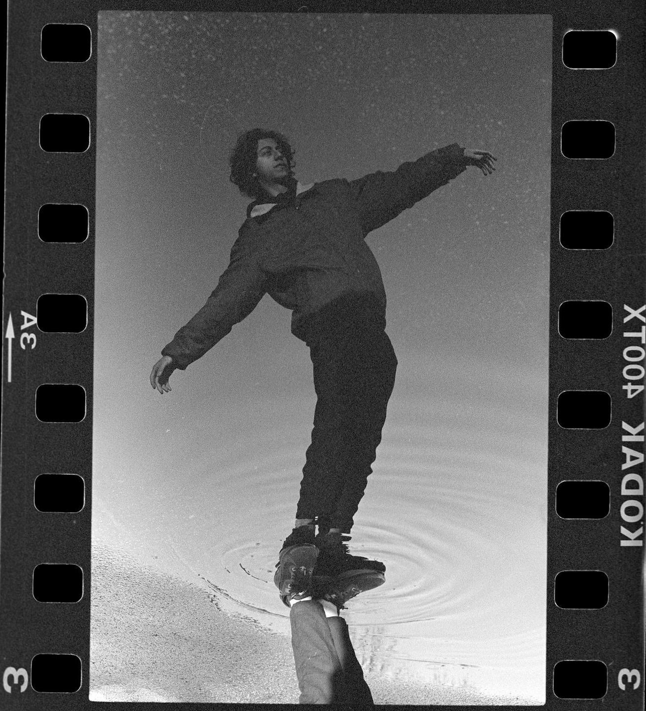 A man balances on one leg in his reflection in a puddle.
