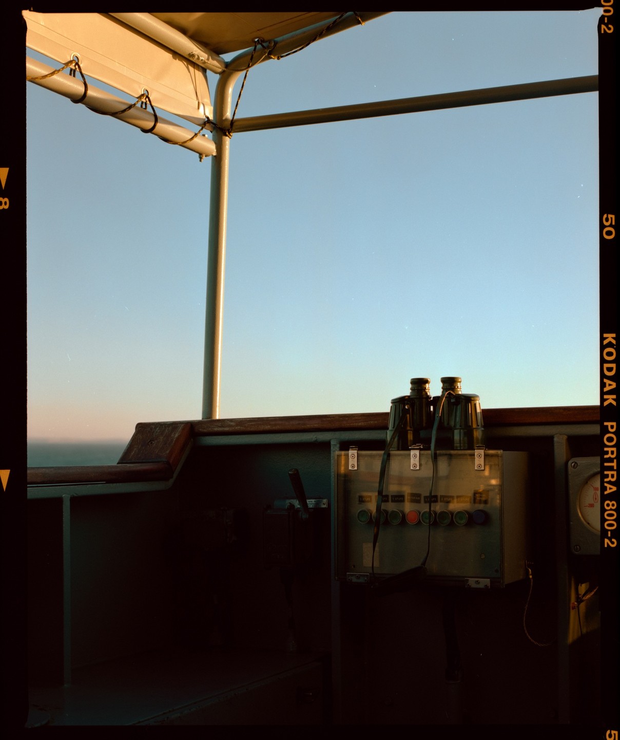 Binoculars rest on a control panel on a boat at sea under a clear sky.