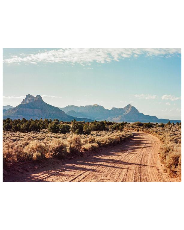 A dirt road leads through a desert landscape towards mountains under a blue sky.
