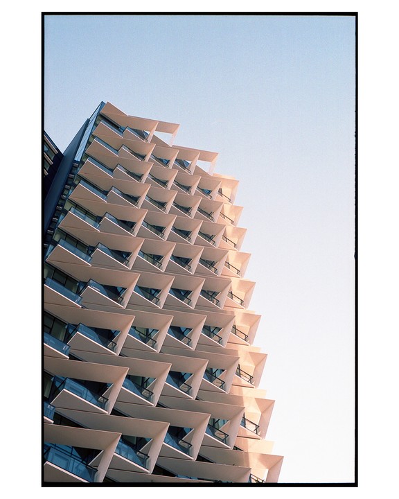 A modern building with triangular balconies is photographed from a low angle against a clear sky.