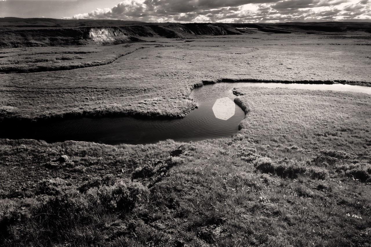 A river winds through a vast, grassy landscape under a cloudy sky.