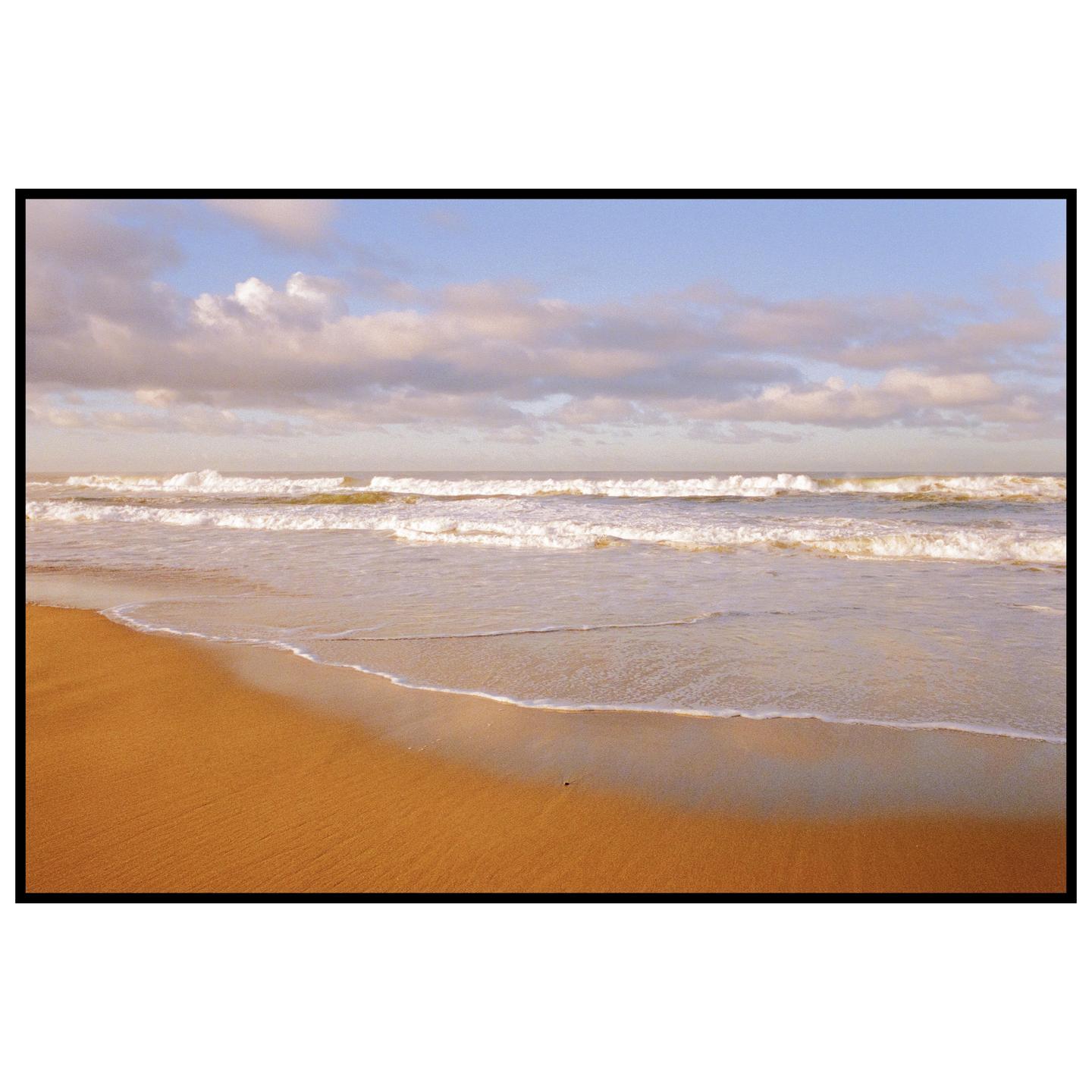 Waves crash on a sandy beach under a cloudy sky.