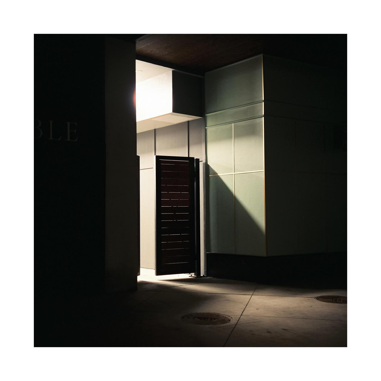 A dark alleyway with a partially open door revealing a bright light source.