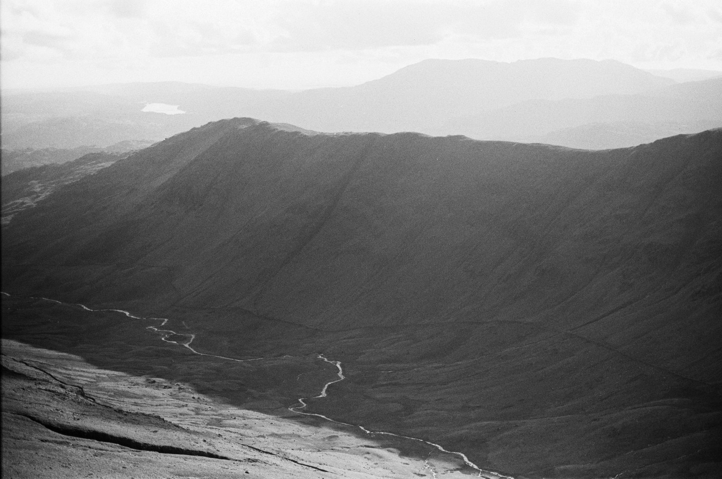 A winding river meanders through a valley between mountains under a hazy sky.
