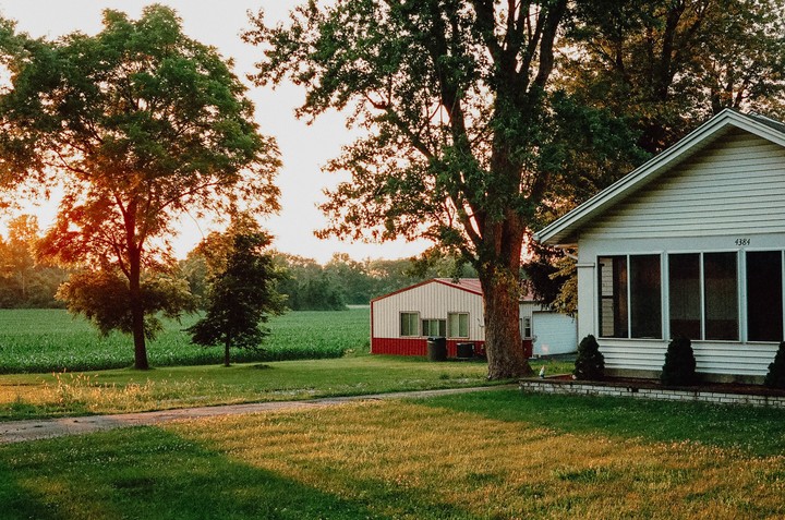 A white house and a red barn are visible behind trees and a green field at sunset.