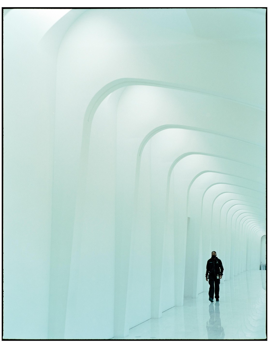 A man walks down a long, arched hallway with a reflective floor.