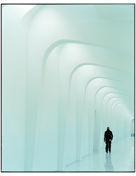A man walks down a long, arched hallway with a reflective floor.