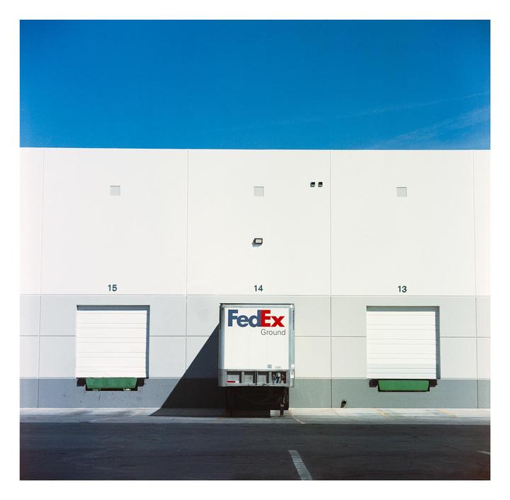 A FedEx truck is parked at a loading dock under a clear blue sky.