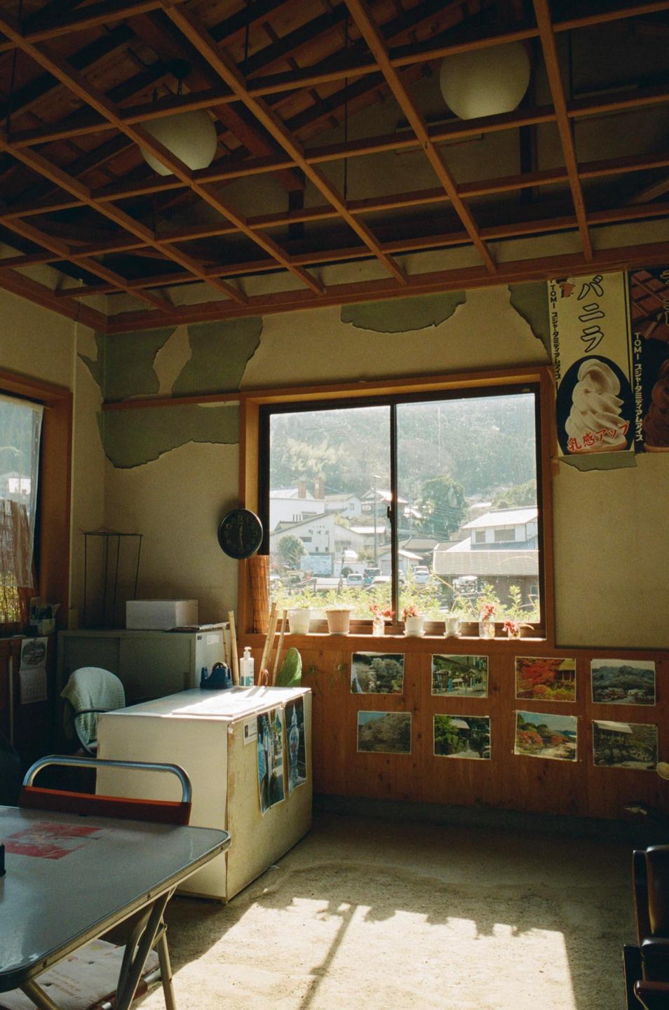 A room with peeling paint on the walls and a wooden lattice ceiling looks out onto a village.