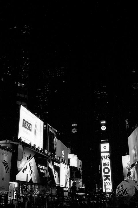 A street scene at night shows numerous illuminated billboards and signs, with dark buildings and sky above.