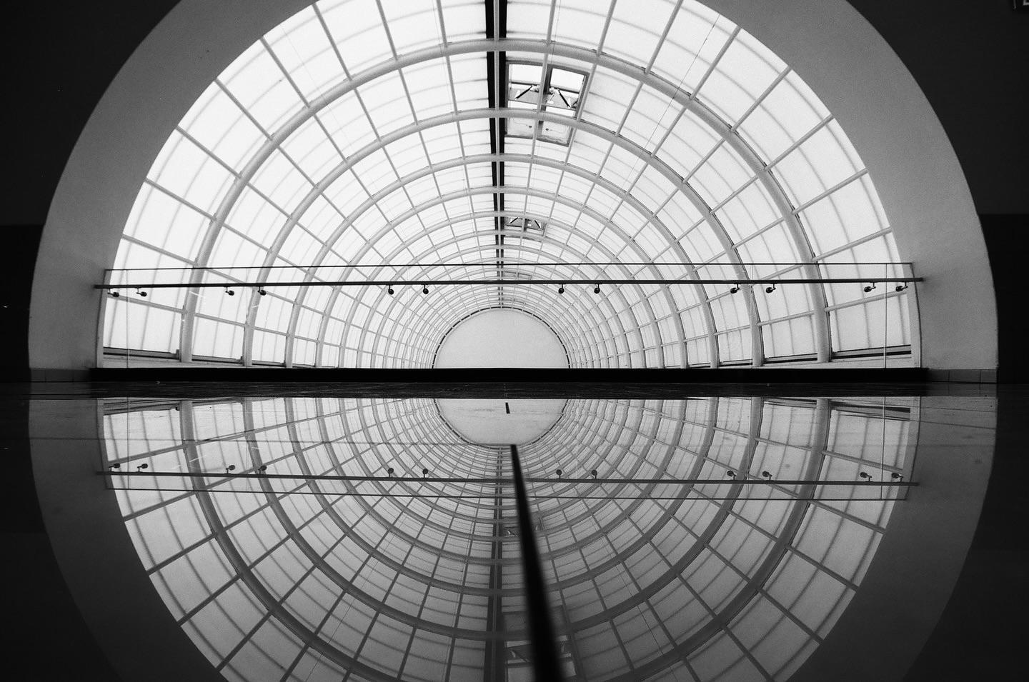 A long, arched, gridded skylight is reflected in the shiny floor below.