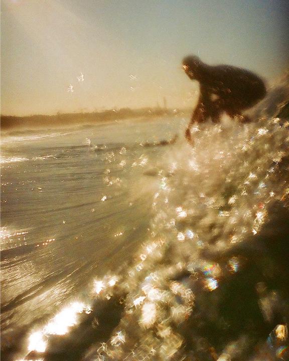 A surfer is riding a wave with golden light reflecting off the water.