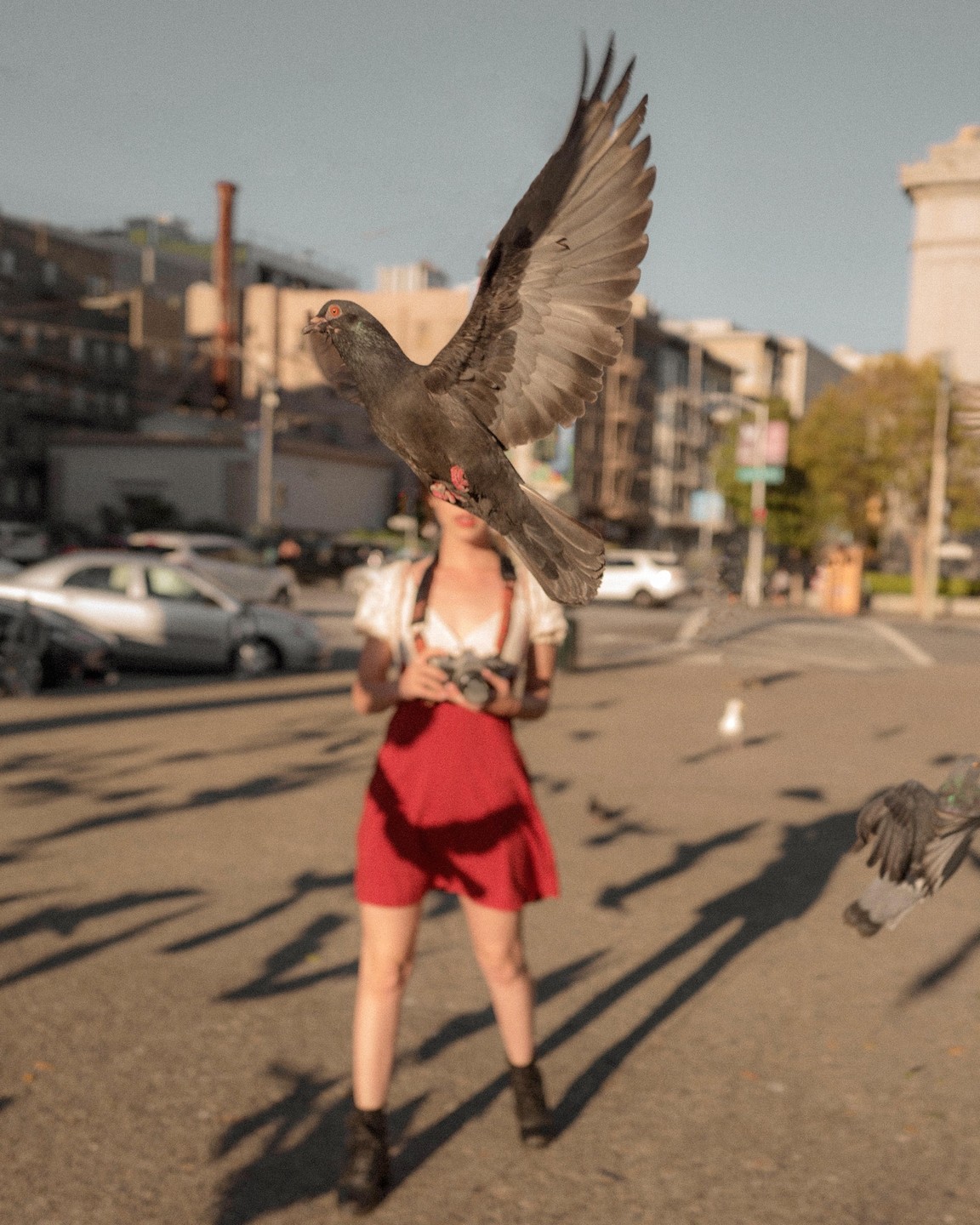 A pigeon flies in front of a woman holding a camera on a city street.