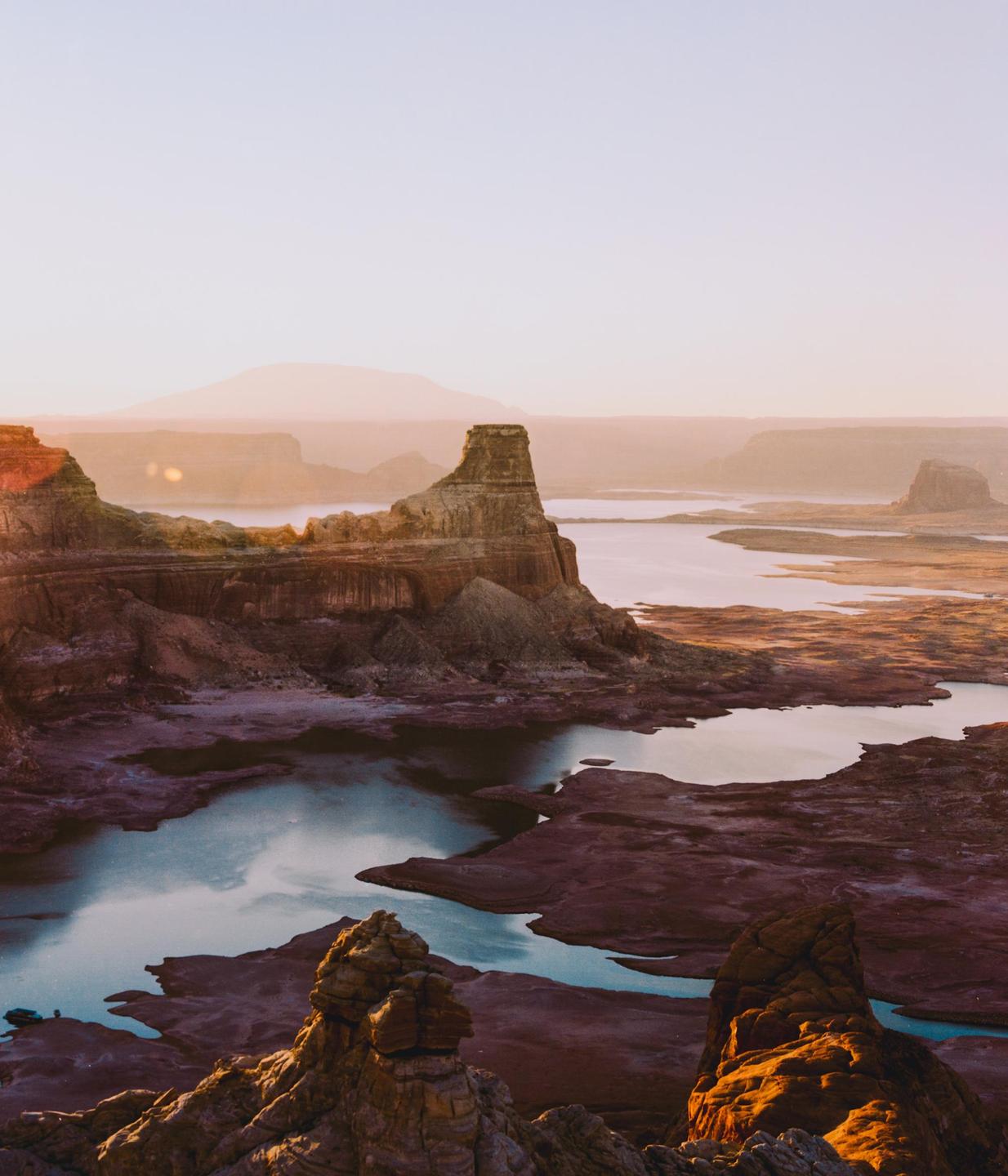 A vast landscape of rock formations and water is illuminated by the rising sun.