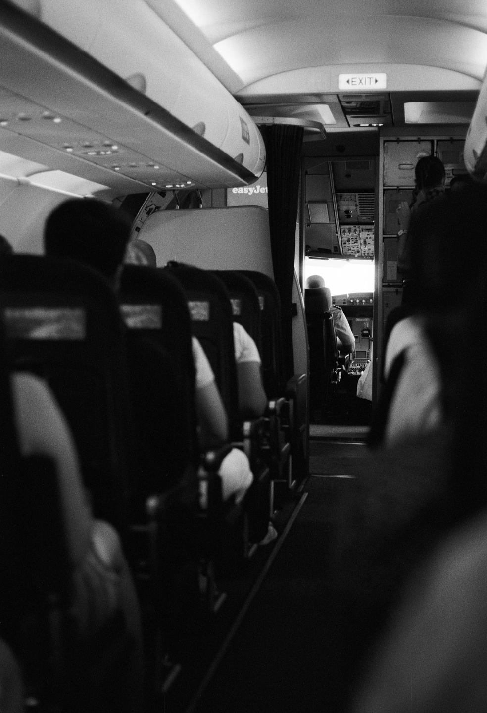 The interior of an airplane shows passengers seated and the cockpit visible at the front.