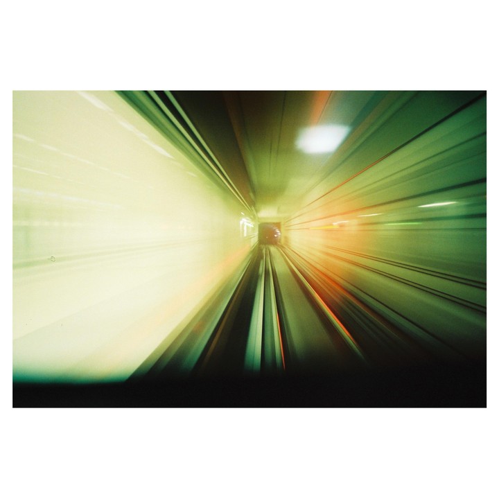 The view from the front of a subway shows the tracks and tunnel with motion blur.