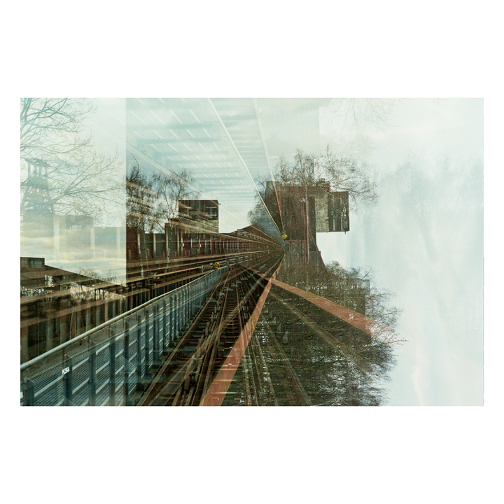 A double exposure shows a train track curving through an urban landscape with bare trees and buildings.