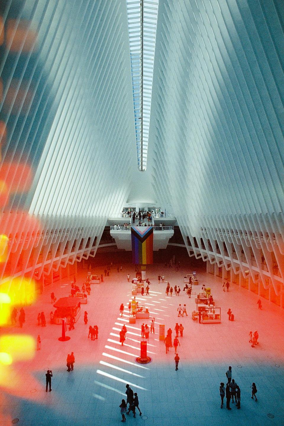 A large, modern interior space with a high, ribbed ceiling and many people walking on the floor below.
