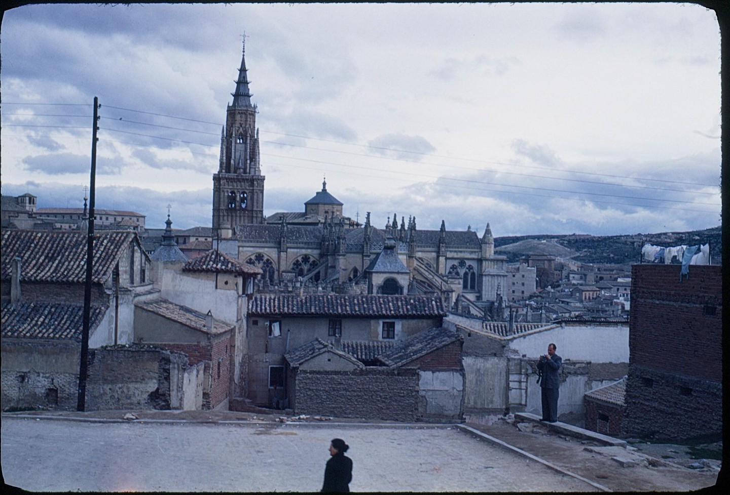 A man and a woman stand on a hill overlooking a city with a large cathedral.