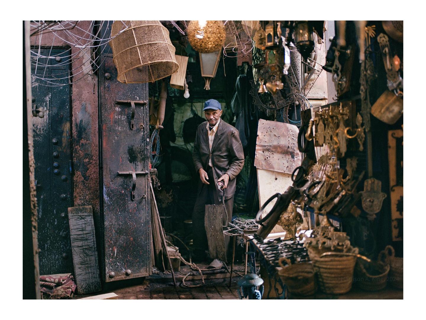 A man stands in a cluttered doorway surrounded by various hanging objects and metalwork.